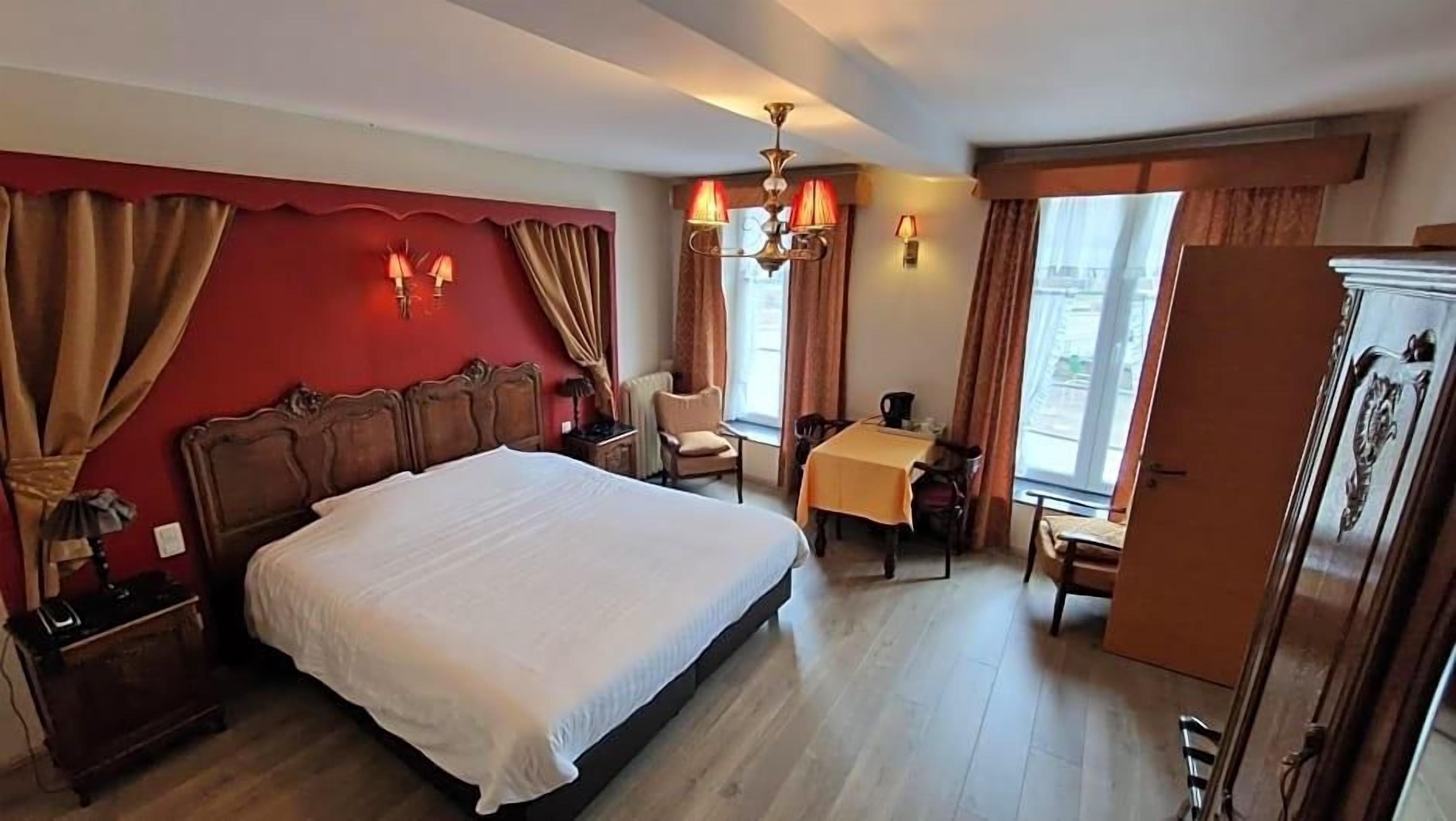 A hotel room with a large bed, a desk with a chair, a wardrobe, and a window with curtains.