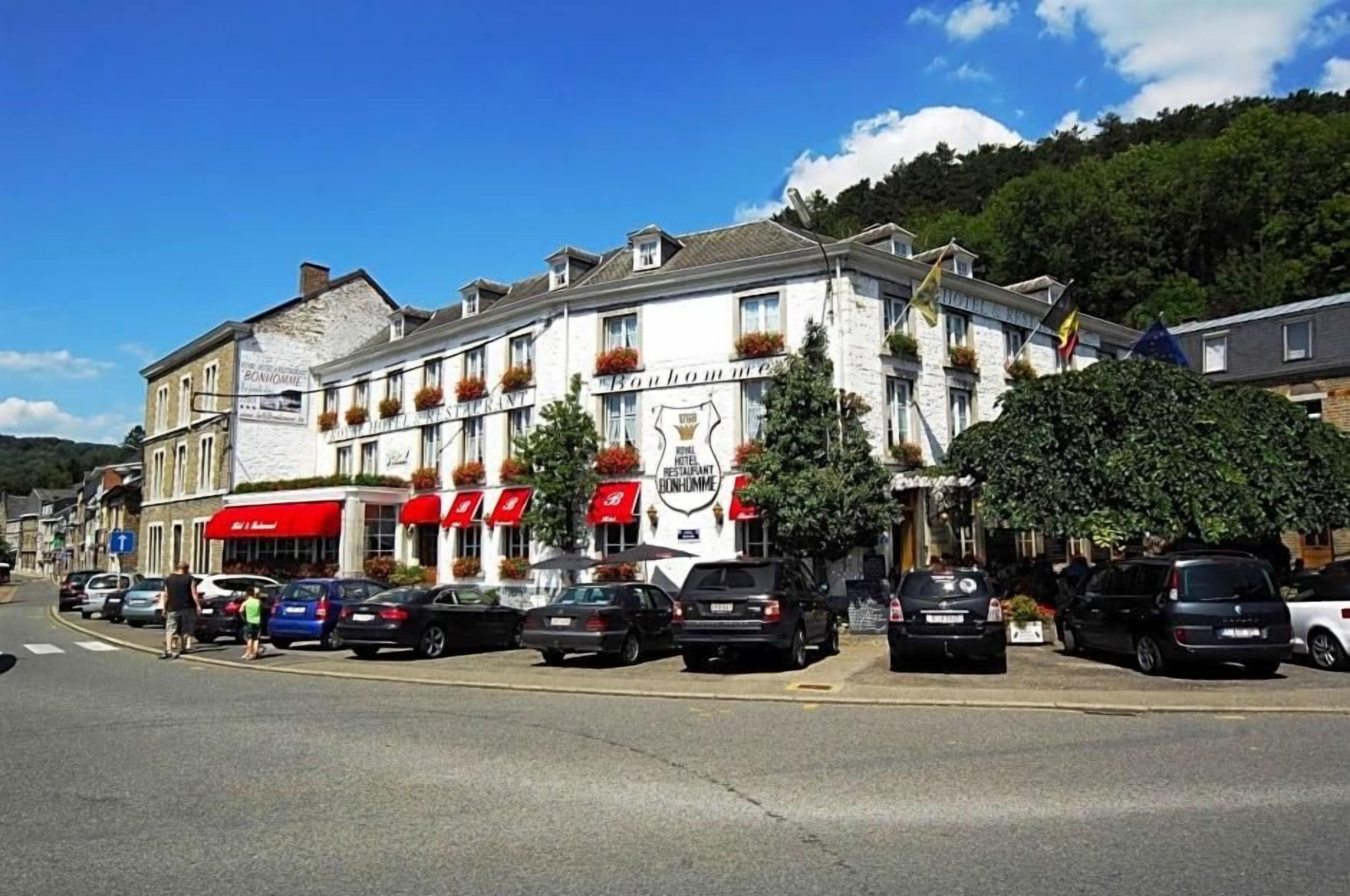 Un bâtiment avec une enseigne indiquant la présence d’un restaurant et d’un hôtel. Des voitures sont garées devant, et un piéton traverse la rue.