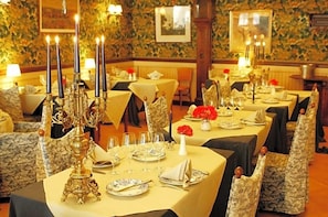 A dining area with tables set for a meal, featuring ornate candle holders and floral centerpieces.