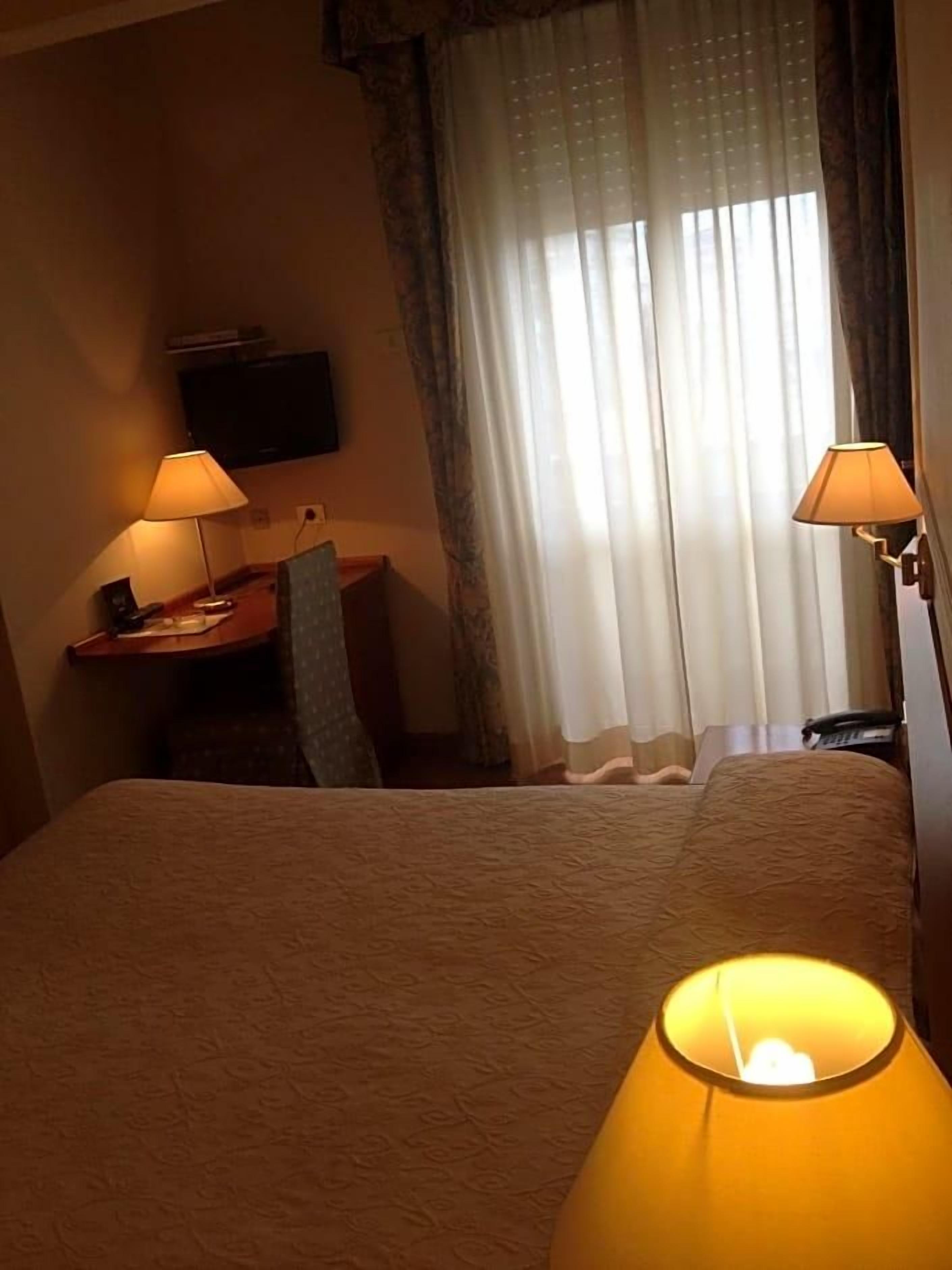 Une chambre d’hôtel avec un lit, deux lampes de chevet, un bureau avec une chaise et un téléviseur fixé au mur.