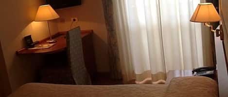 Una habitación de hotel con cama, dos lámparas de noche, un escritorio con silla y un televisor en la pared.