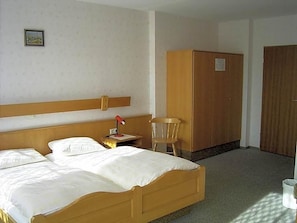 A hotel room with a double bed, a wooden wardrobe, a small table with a lamp, and a chair. - Hotel Sonnenhof (Thannhausen)