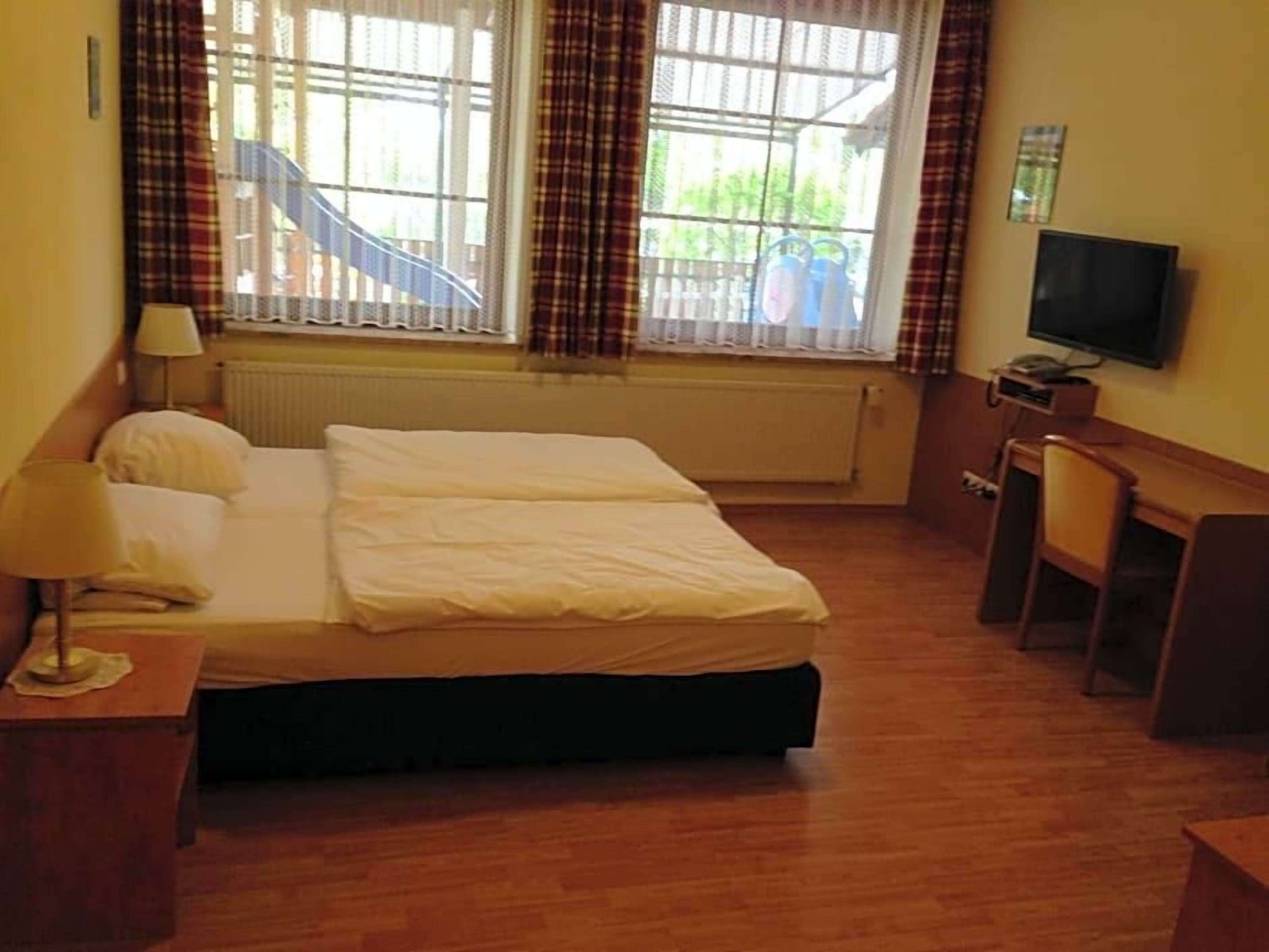 A hotel room with a bed, a desk, a chair, a television, and a window with curtains.