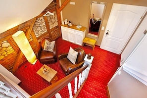 Una habitación con alfombra roja, escalera de madera, pared de piedra, armario blanco, espejo y puerta.