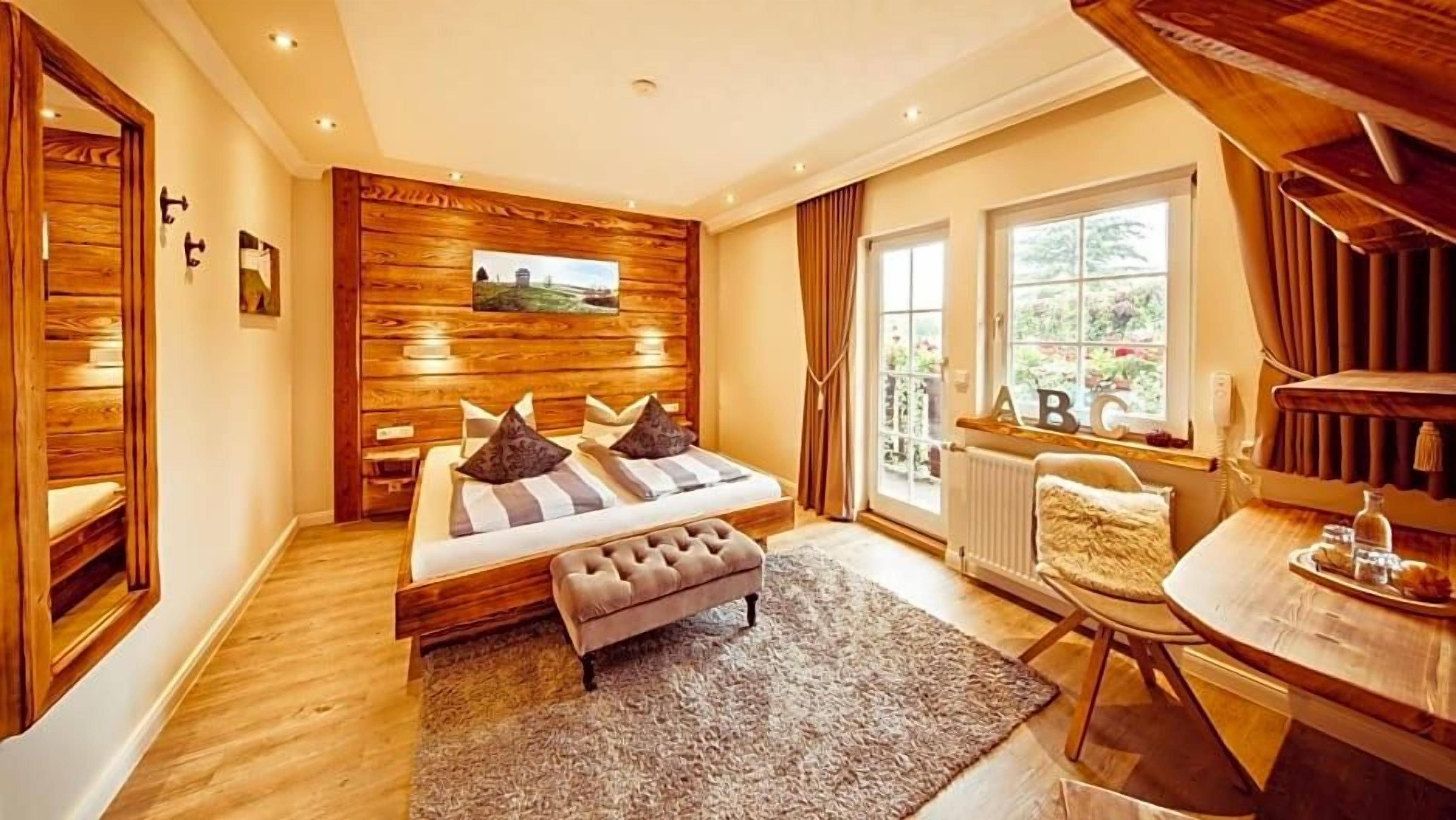 A bedroom with a wooden wall panel, a bed with pillows, a bench, a window with curtains, and a table with a tray.