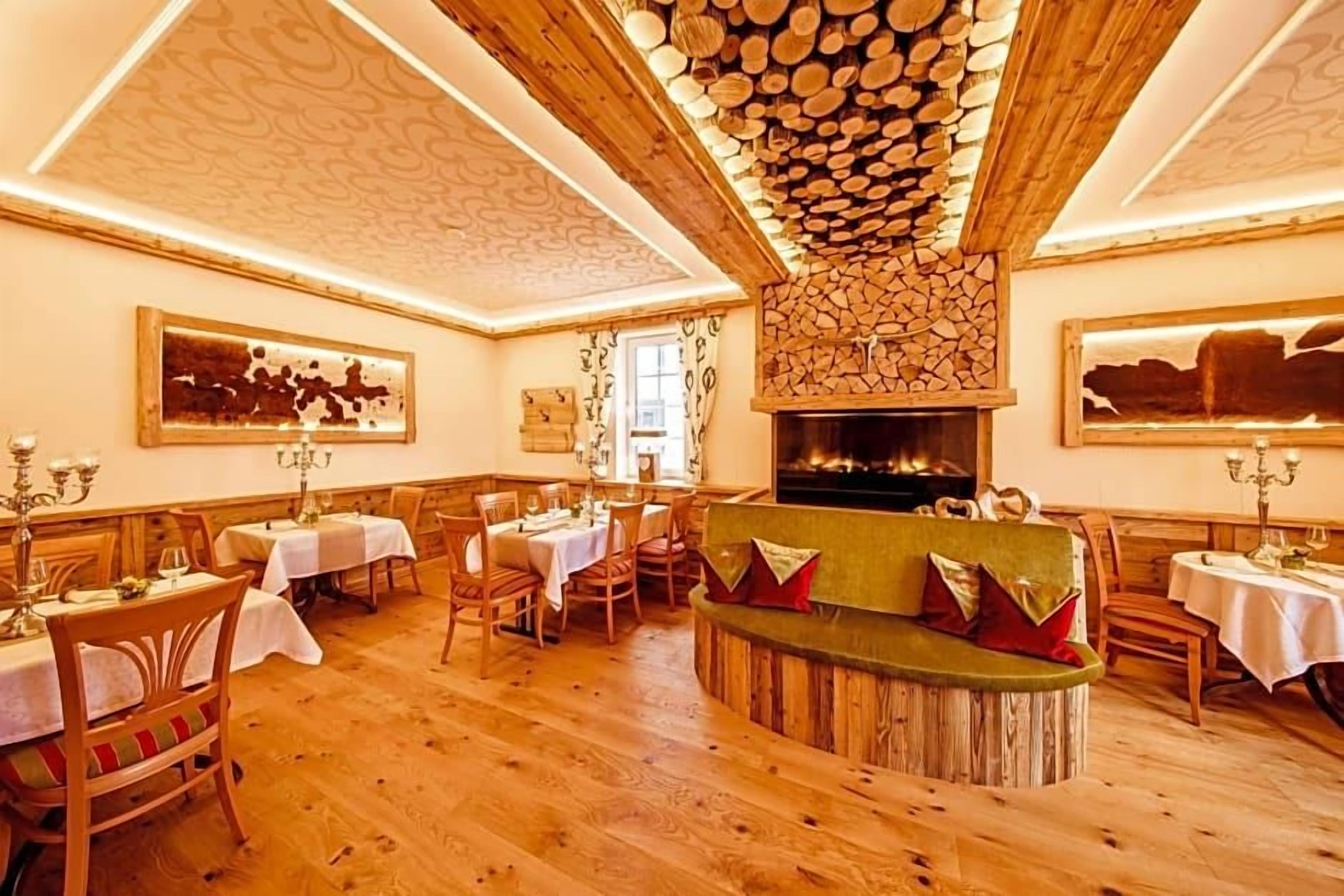 A dining area with wooden tables and chairs, a central seating area with cushions, and a fireplace.