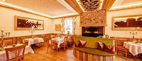 A dining area with wooden tables and chairs, a central seating area with cushions, and a fireplace.