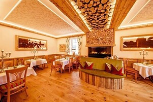 Un comedor con mesas y sillas de madera, un espacio central con cojines y una chimenea.