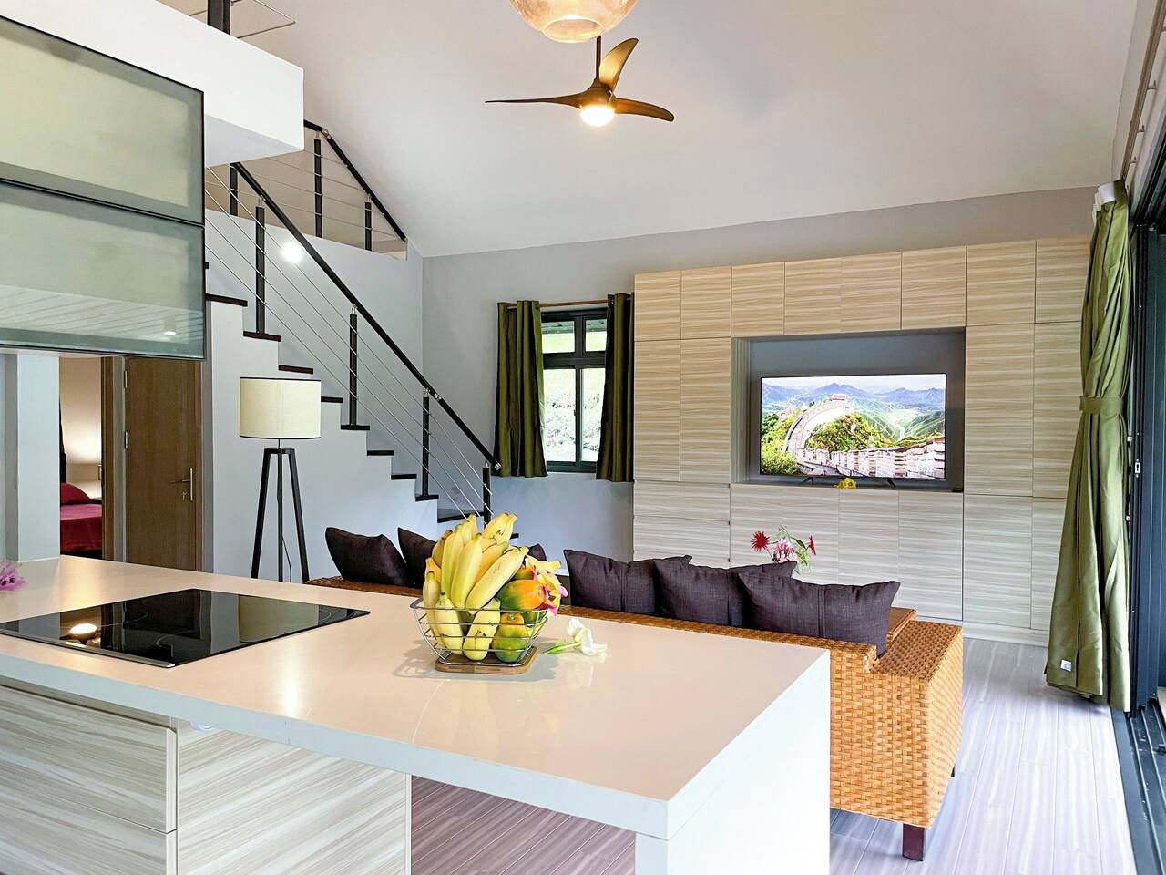 A modern living space with a kitchen island, a dining area, a sofa, and a television mounted on the wall.