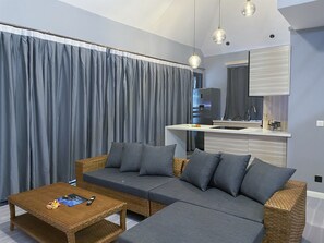 Ein modernes Wohnzimmer mit einer Couch, einem Couchtisch und einer Küchenzeile inklusive Kühlschrank und Spüle.