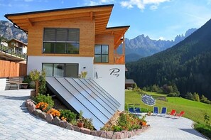 Un chalet moderno con techo inclinado, fachada de madera y balcón con vistas a un paisaje montañoso.