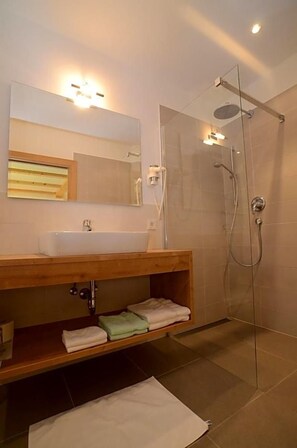 Un baño moderno con cabina de ducha de vidrio, tocador de madera con lavabo y un espejo arriba.