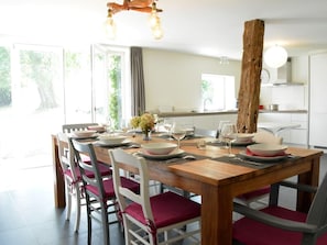 A dining area with a wooden table, white chairs with red cushions, and a large window with curtains. - Beautiful Ardennes House In Quiet Area (Sainte-Ode)