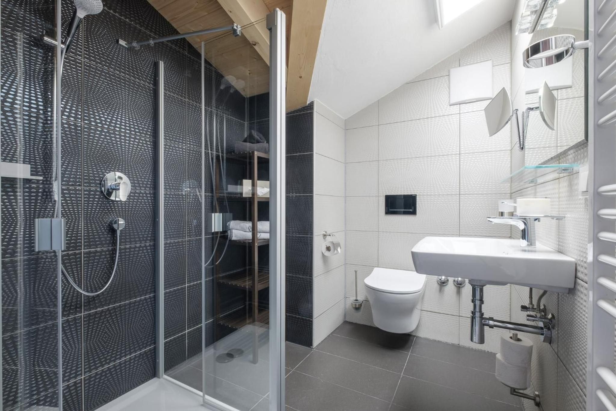 Ein modernes Badezimmer mit einer Duschkabine, einem weißen Waschbecken und einer Toilette.