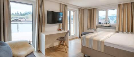 A modern hotel room with a bed, a desk, a chair, and a TV.
