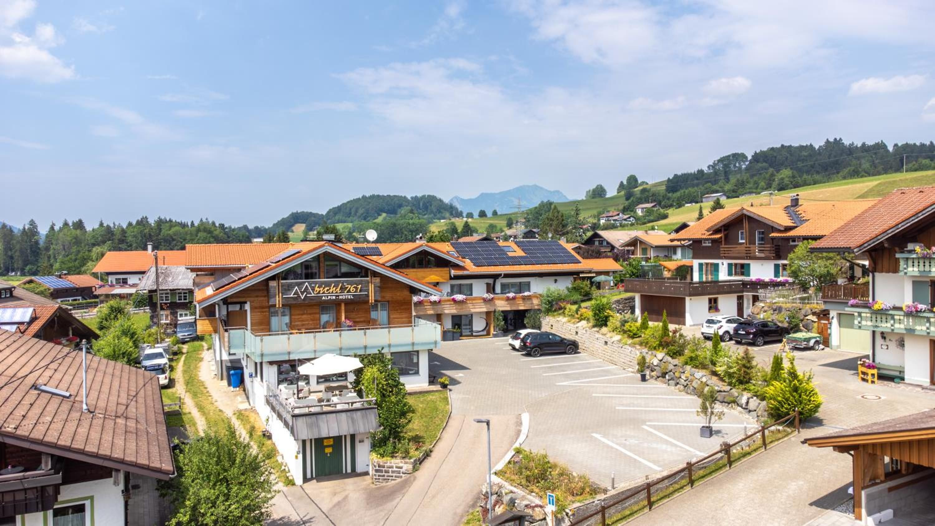 Un hotel con un cartel que dice 'Bichl 761 Alpin-Hotel' en un entorno rural, con estacionamiento y casas aledañas.