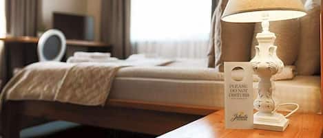 Habitación de hotel con una cama, una mesita de noche con lámpara, un espejo y un cartel que dice 'NO MOLESTAR'.
