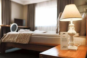 Habitación de hotel con una cama, una mesita de noche con lámpara, un espejo y un cartel que dice 'NO MOLESTAR'.