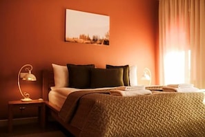 Una habitación de hotel con cama, mesita de noche, lámpara y ventana con cortinas.