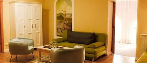Un salón con un sofá verde, dos sillones, una mesa de centro y un cuadro de una jirafa.
