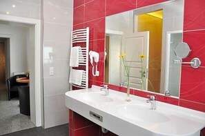 Une salle de bain moderne avec un lavabo blanc, un grand miroir et des murs recouverts de carreaux rouges.