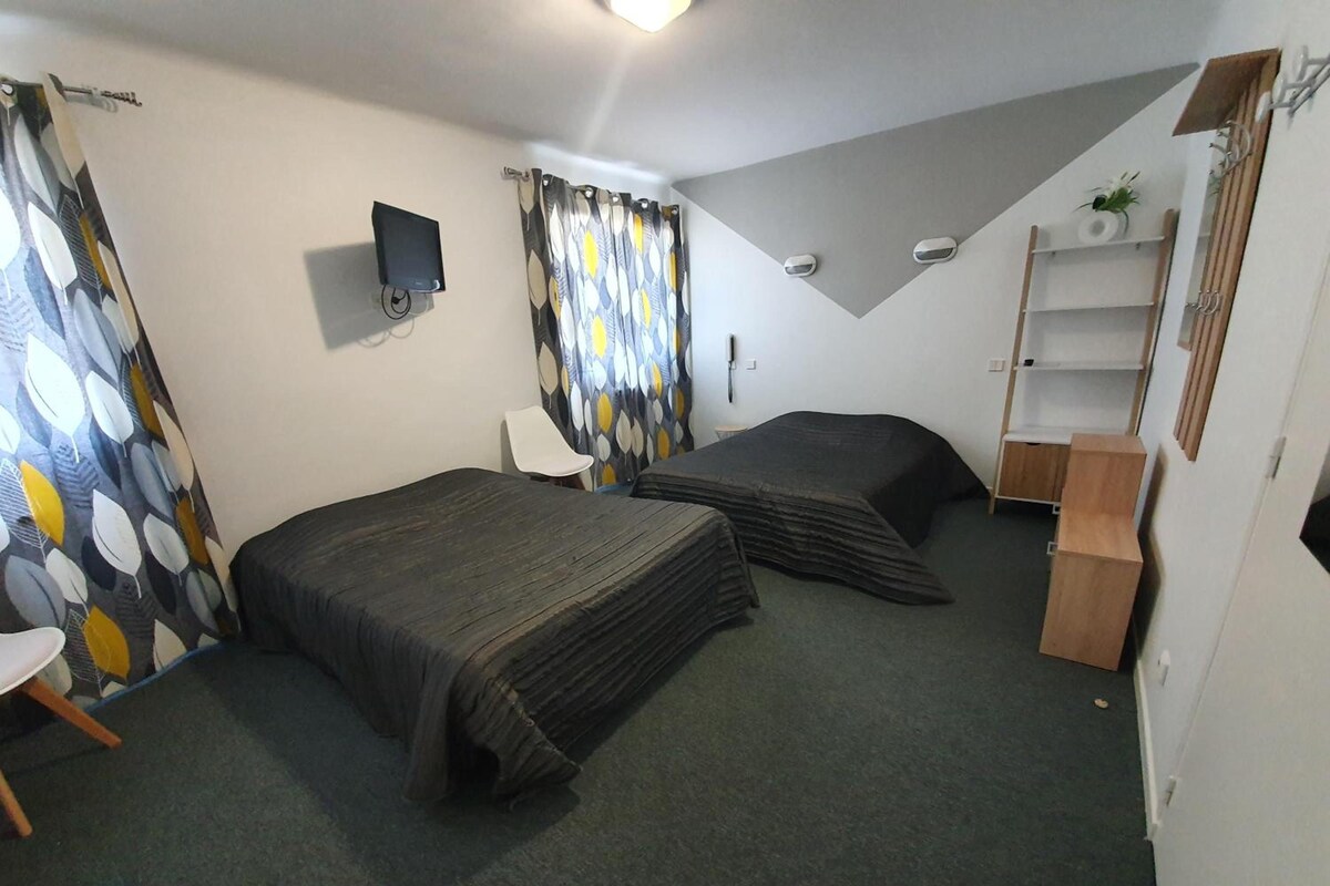 A room with two beds, a desk, a chair, a TV, and a shelf.