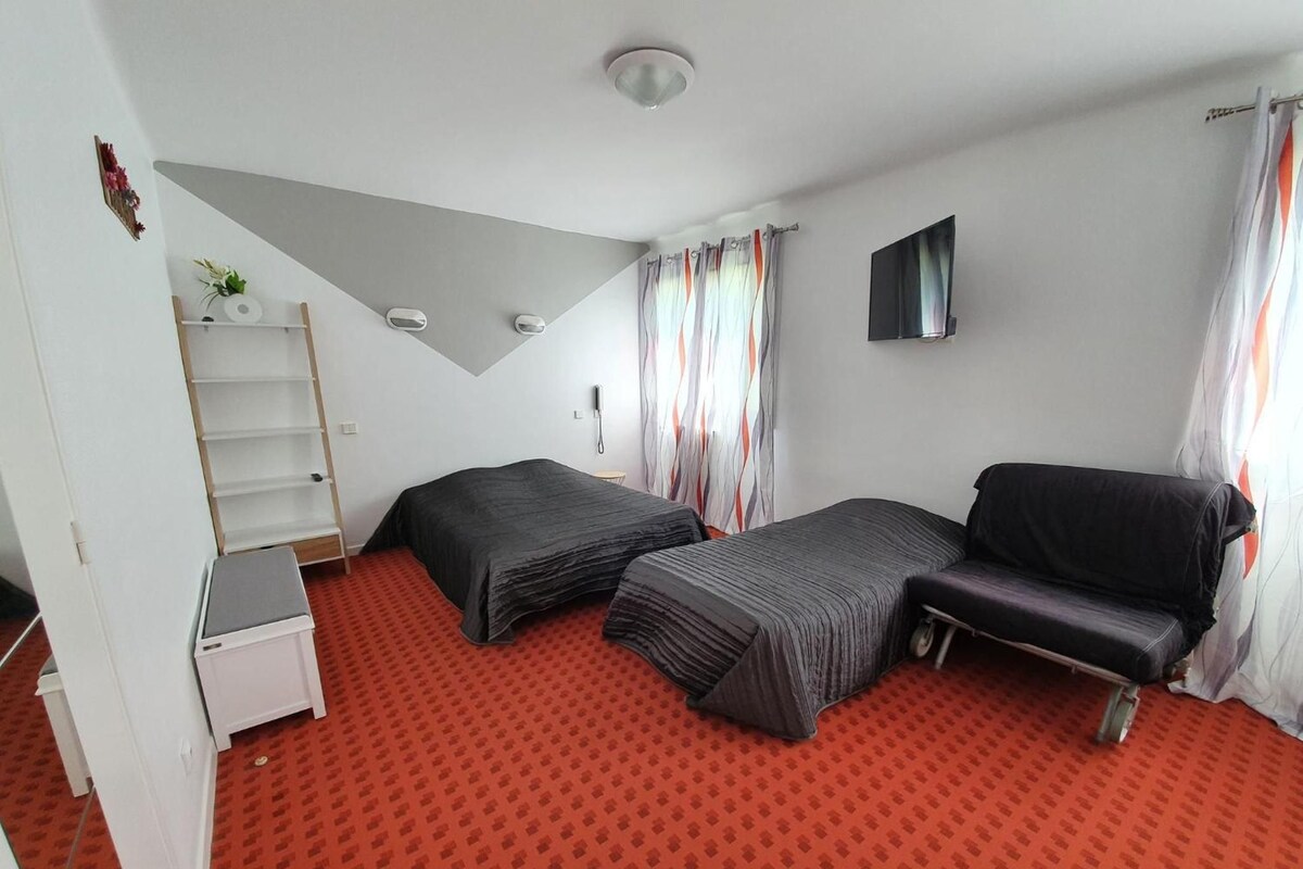 A compact room with two beds, a desk, a chair, a TV, and a window with curtains.