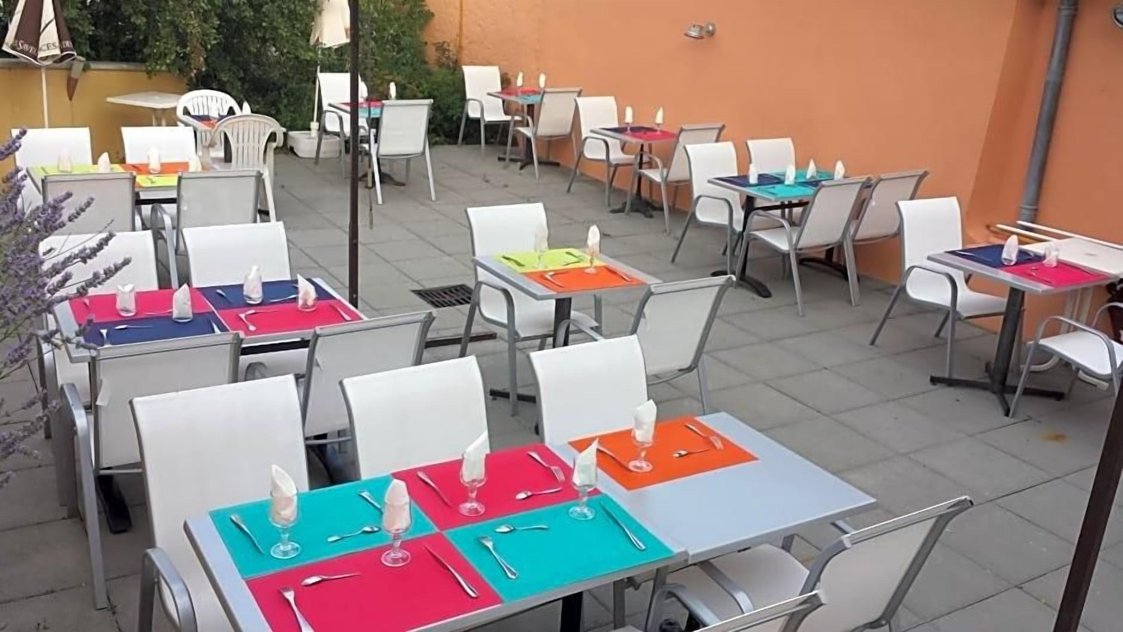 Un patio al aire libre con varias mesas y sillas, algunas con sombrillas.