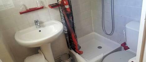 A bathroom with a sink, toilet, shower, and a trash bin.