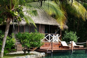 Une structure à toit de chaume dotée d’une terrasse en bois, de chaises longues et d’une piscine.