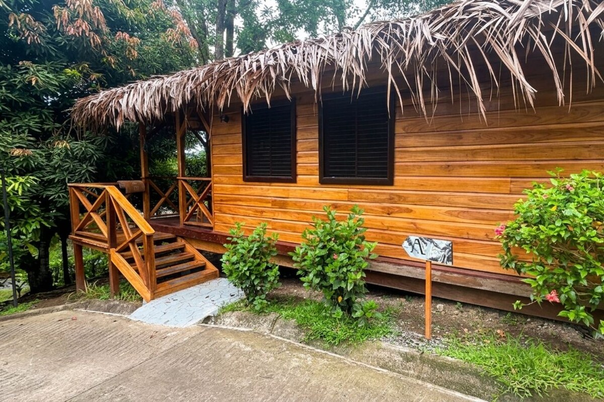 A wooden cabin with a thatched roof, a wooden staircase, and a small garden area.