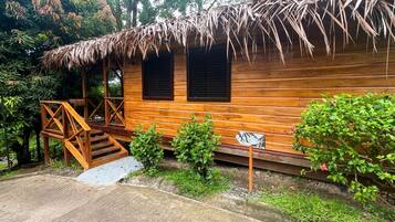 A wooden cabin with a thatched roof, a wooden staircase, and a small garden area.