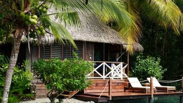 A thatched-roof structure with a wooden deck, lounge chairs, and a pool.