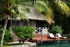 A thatched-roof structure with a wooden deck, lounge chairs, and a pool.