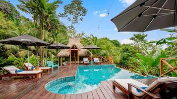 A wooden deck with a swimming pool, lounge chairs, and umbrellas.