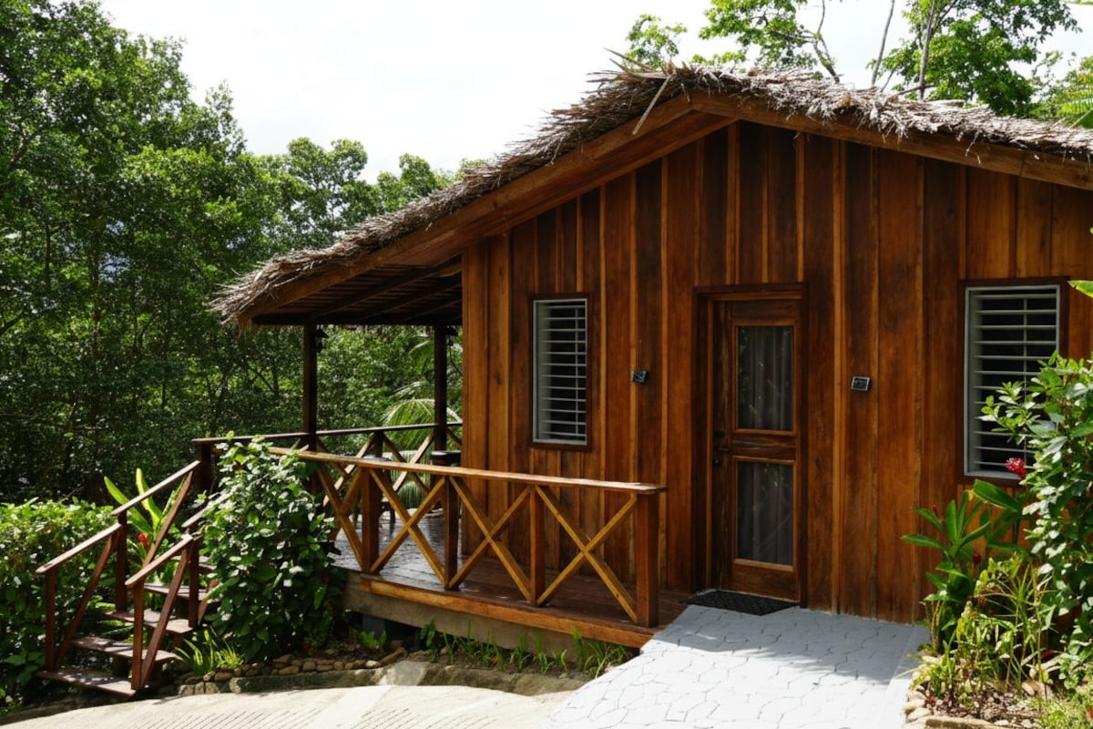 A wooden cabin with a thatched roof, a wooden porch, and a small garden area.