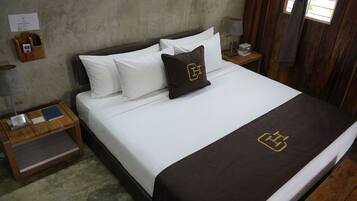 A neatly made bed with white and brown bedding, a wooden nightstand with a lamp and a small table, and a wooden wall.