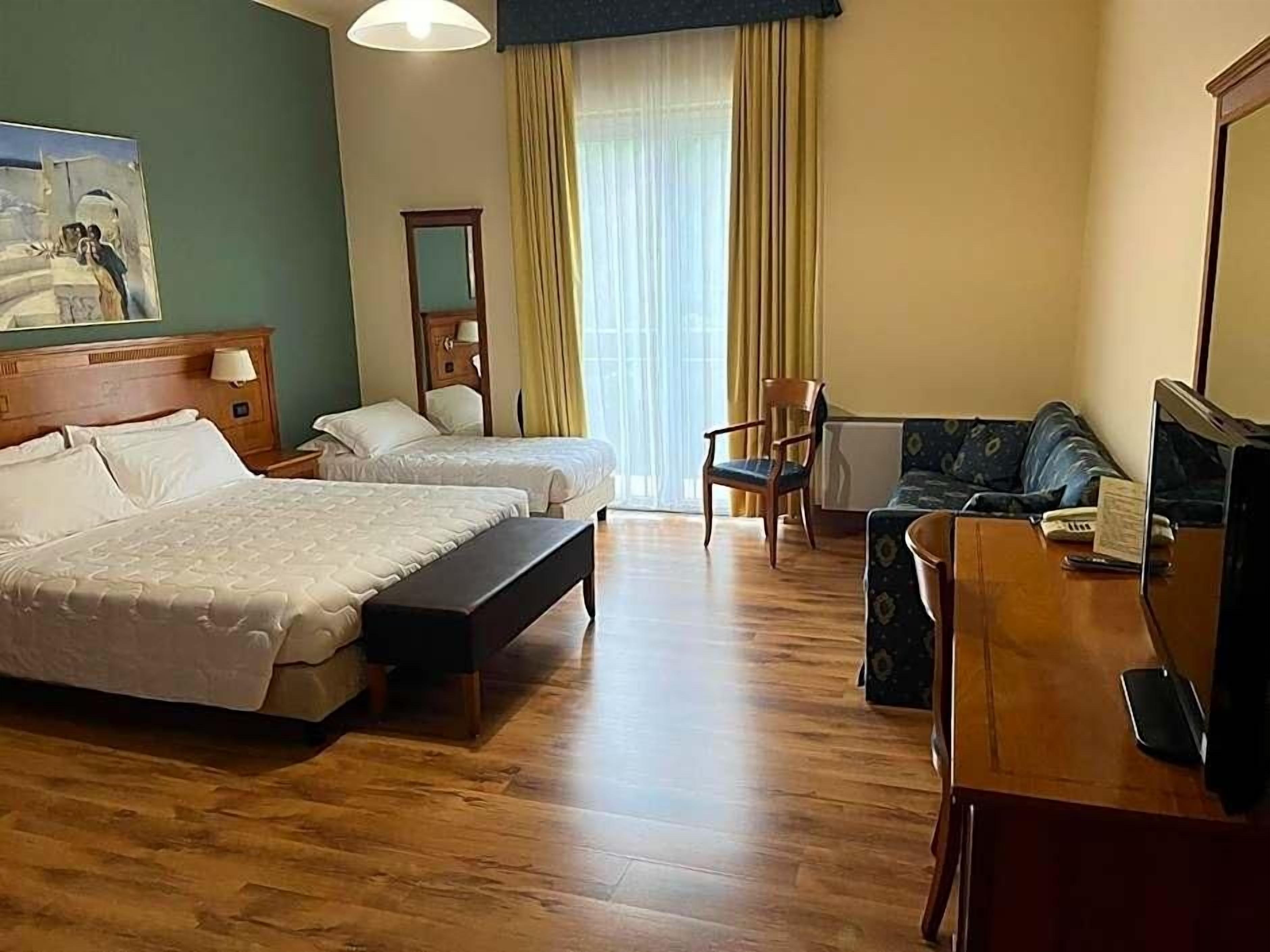 Ein Hotelzimmer mit zwei Betten, einem Schreibtisch mit Telefon, einem Stuhl und einem fensterbepflanzten Fenster.