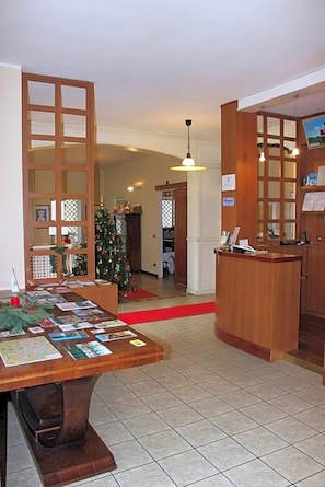 A reception area with a wooden desk displaying brochures, a Christmas tree, and a reception counter. - Hotel De La Ville (Bereguardo)