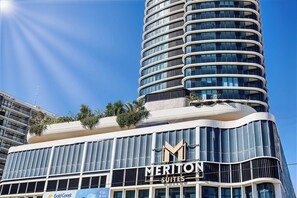 Un hotel moderno con fachada curva, un llamativo letrero de 'Meriton Suites' y un jardín en la azotea.