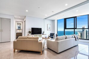 A modern living room with a large TV, two sofas, a dining table, and a view of the ocean. - Paradise Coast Luxe in the heart of Surfers Paradise (Surfers Paradise)