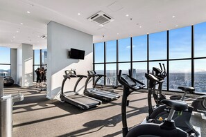 A gym with treadmills, stationary bikes, and exercise balls, with a city view through large windows. - Paradise Coast Luxe in the heart of Surfers Paradise (Surfers Paradise)