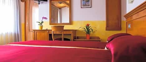 Quarto de hotel com uma cama grande, uma escrivaninha de madeira, um espelho e um guarda-roupa.