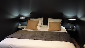 Un llit amb un capçal fosc, dues taules de nit amb làmpades i una ampolla d'aigua a cadascuna.