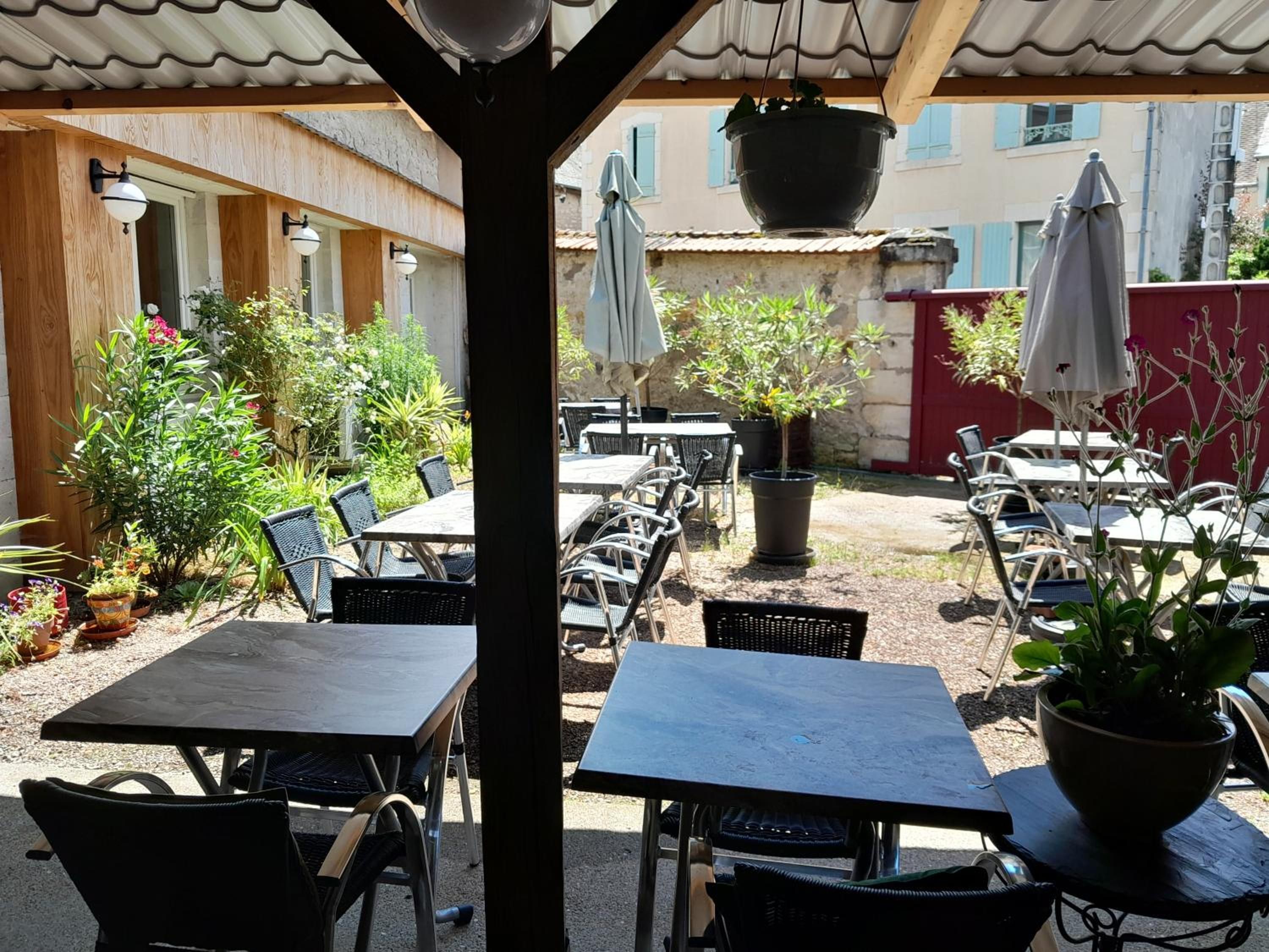 Un patio al aire libre con mesas y sillas, rodeado de plantas en macetas y sombrillas.