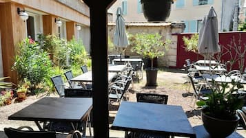 Une terrasse extérieure avec des tables et des chaises, entourée de plantes en pot et d’ombrelles.