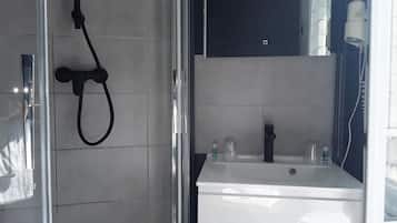 Une salle de bain avec une douche à parois de verre, un lavabo blanc et un meuble de rangement de couleur foncée au-dessus du lavabo.
