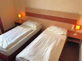 A hotel room with two beds, each with a pillow and a nightstand with a lamp.