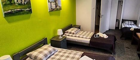 Ein Hotelzimmer mit zwei Betten, einem Schreibtisch und einem Sessel. An den Wänden befinden sich Gemälde und eine Klimaanlage.