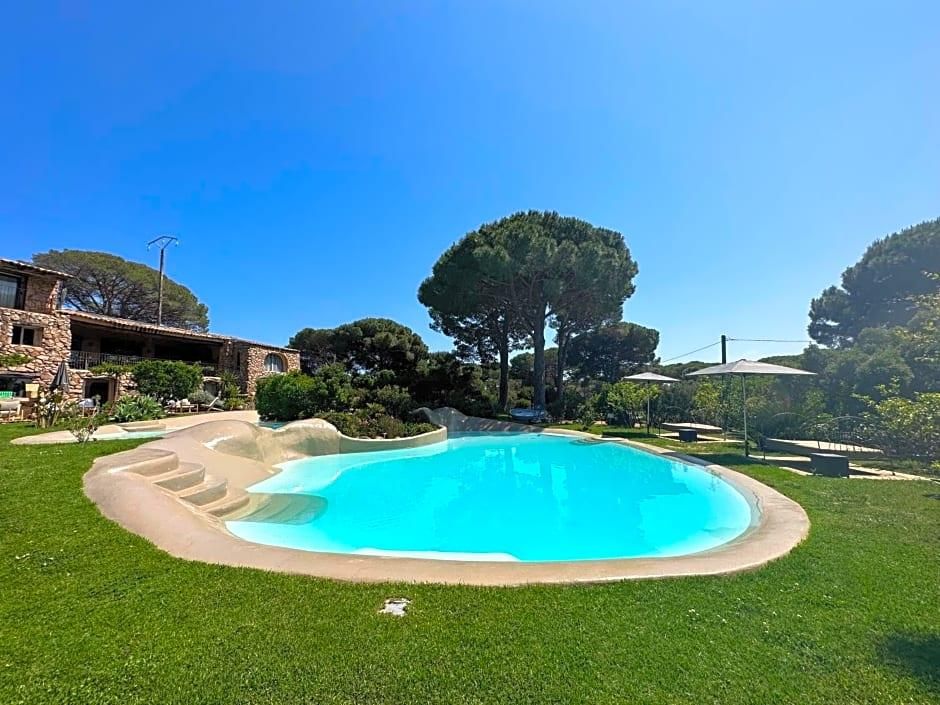 Une piscine bordée de pierres, entourée d’une pelouse bien entretenue, avec un bâtiment en pierre et des arbres en arrière-plan.